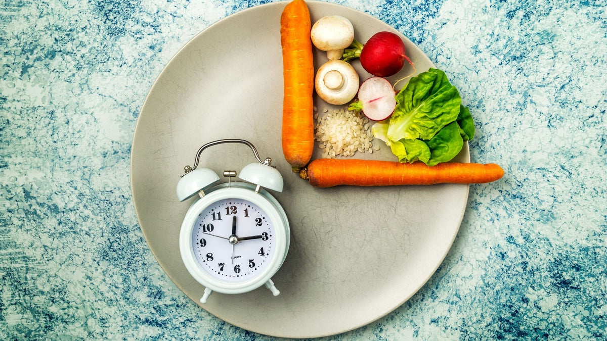 Plato con verduras formando un reloj junto a un despertador, representando el ayuno intermitente y la alimentación consciente.