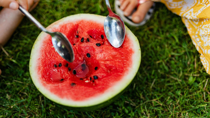 Personas compartiendo una sandía fresca cortada por la mitad sobre el pasto