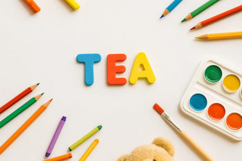 Escritorio infantil con lápices de colores, témperas y la palabra TEA al centro, representando el aprendizaje y apoyo en el Trastorno del Espectro Autista.