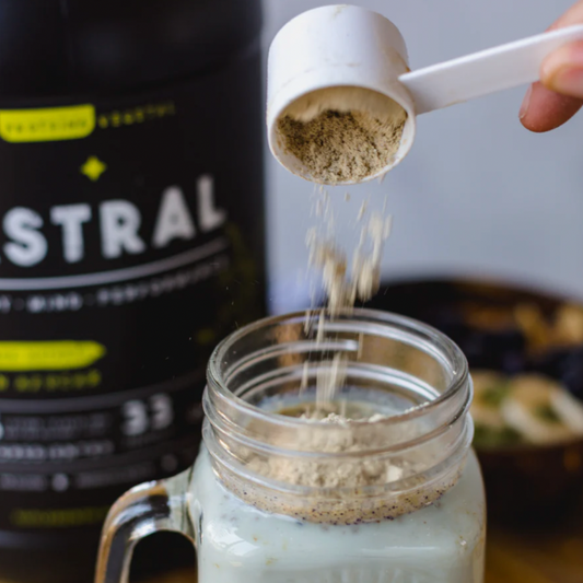 Vaso de vidrio con Proteína Lupino Natural Astral en polvo junto a cuchara de plástico, frasco Astral de fondo, 910 gramos, Ortomolecular Chile